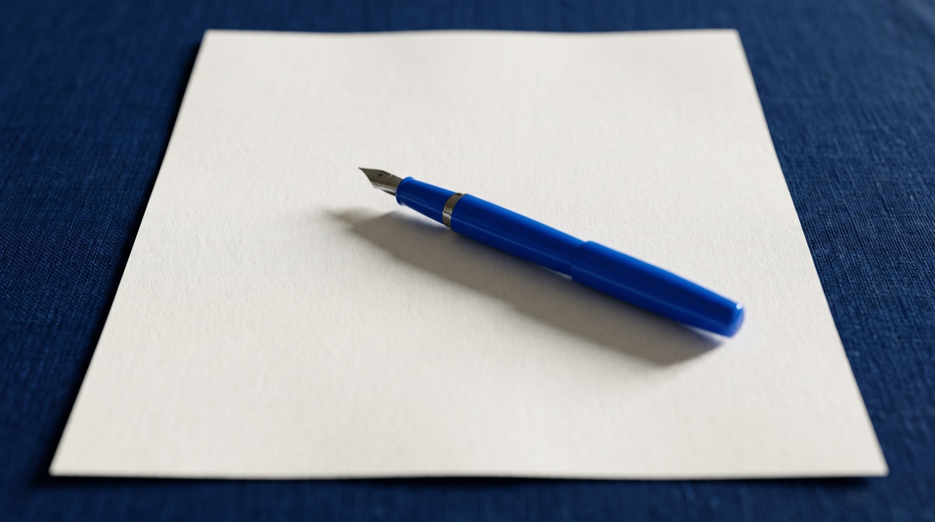A blank sheet of paper-white contract stock on a navy table with a blue fountain pen