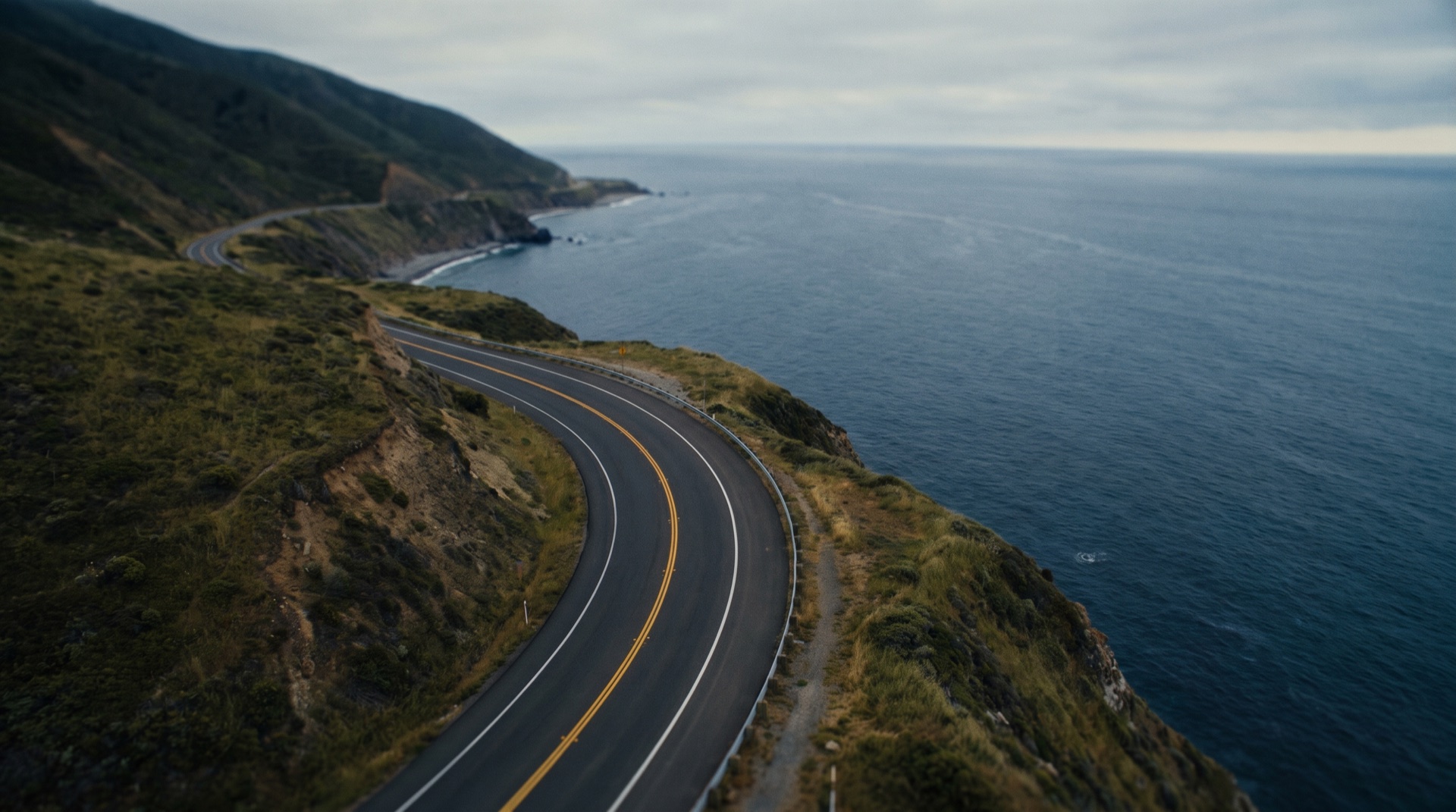 Aerial view at golden hour of an empty coastal road meeting a calm navy sea