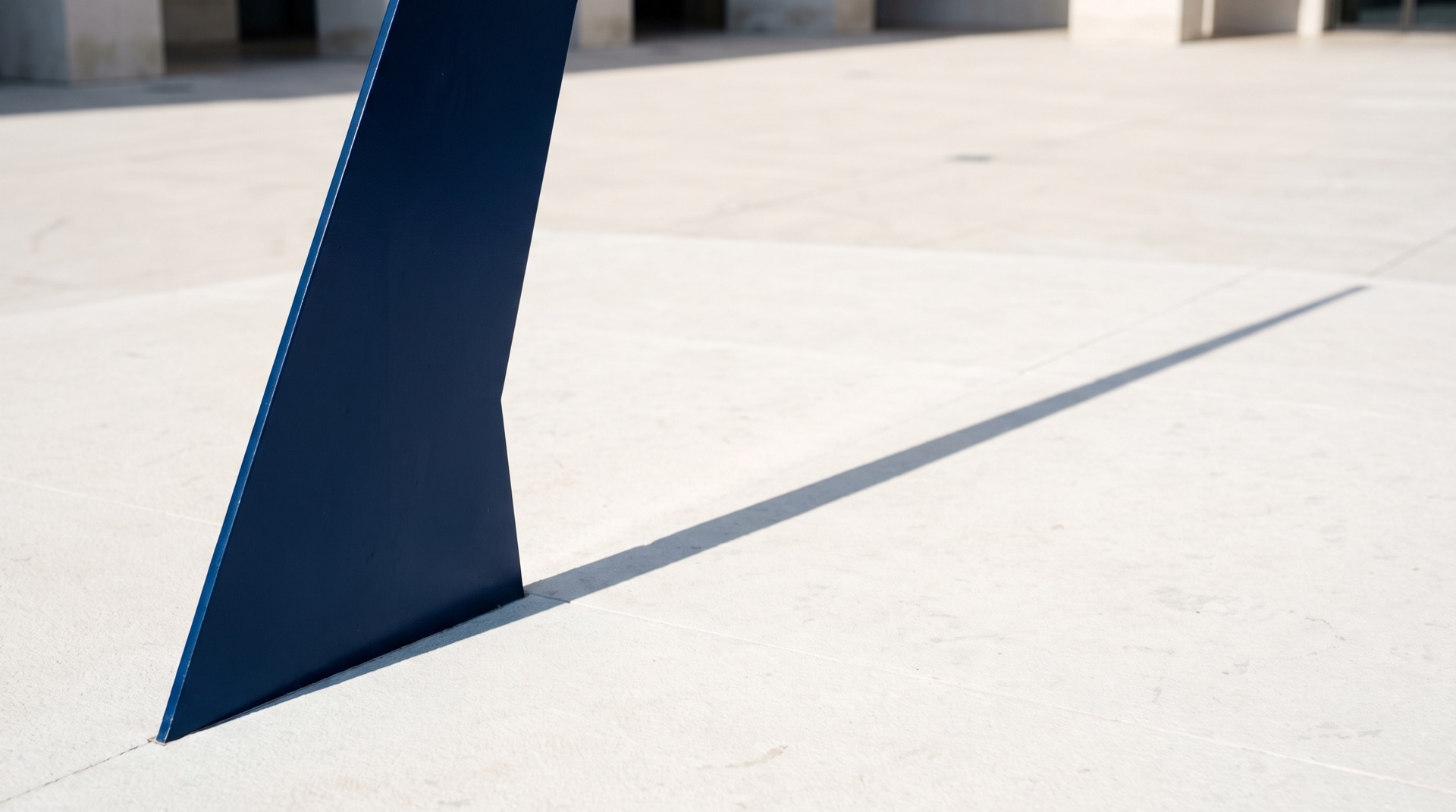 A navy sundial blade casting one long shadow across a pale stone plaza at dawn